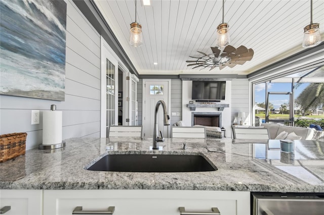 kitchen featuring light stone countertops, sink, white cabinets, and decorative light fixtures