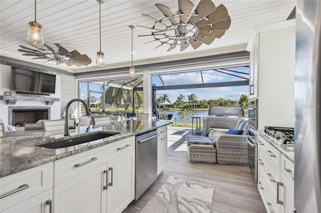 kitchen with white cabinets, sink, dark stone countertops, decorative light fixtures, and stainless steel appliances