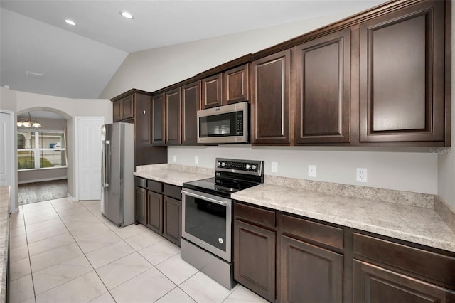 kitchen with dark brown cabinetry, stainless steel appliances, a notable chandelier, lofted ceiling, and light tile patterned flooring