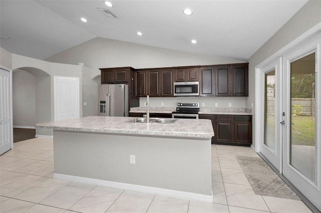 kitchen with sink, an island with sink, lofted ceiling, light tile patterned floors, and appliances with stainless steel finishes