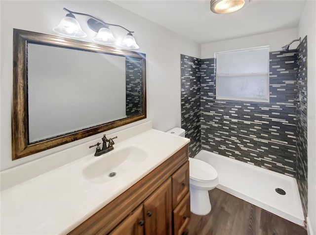 bathroom featuring hardwood / wood-style flooring, vanity, toilet, and tiled shower