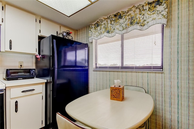 kitchen with backsplash, black refrigerator, white cabinets, and breakfast area