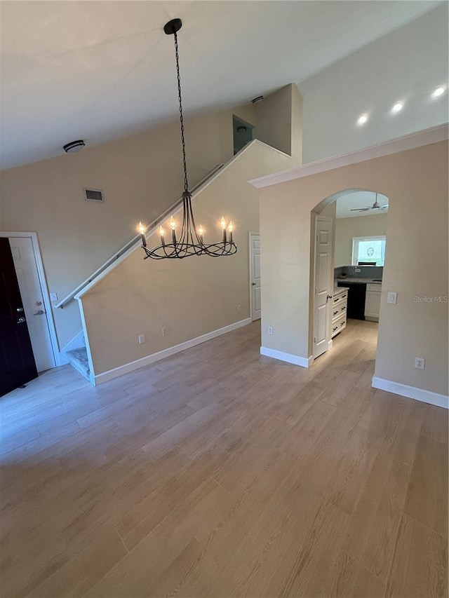 unfurnished dining area featuring an inviting chandelier, high vaulted ceiling, and light hardwood / wood-style floors