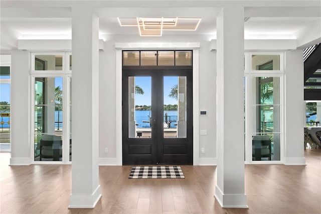 foyer featuring a healthy amount of sunlight, a water view, wood-type flooring, and french doors