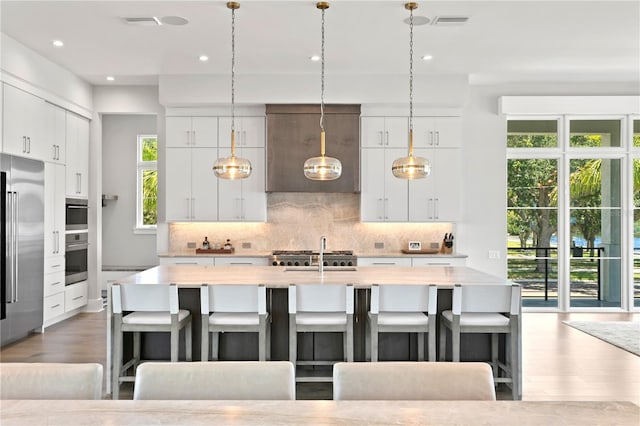 kitchen featuring white cabinets, a kitchen island with sink, and hanging light fixtures