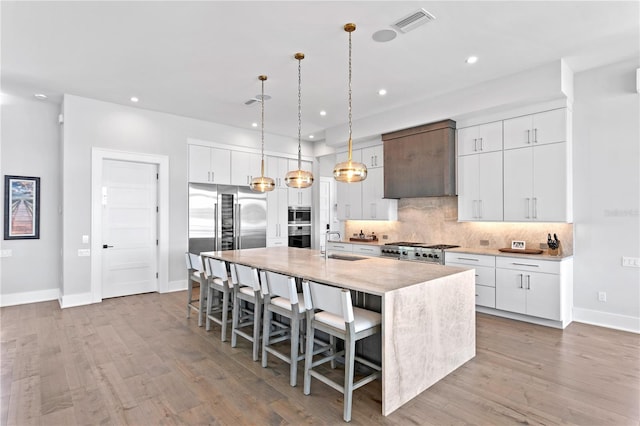 kitchen with a center island with sink, white cabinets, light wood-type flooring, and stainless steel appliances