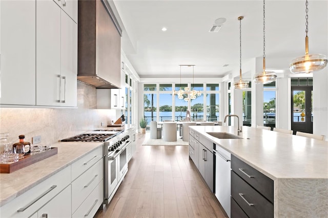 kitchen with white cabinetry, wall chimney exhaust hood, decorative light fixtures, appliances with stainless steel finishes, and light wood-type flooring