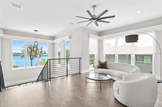 living room featuring hardwood / wood-style floors, ceiling fan with notable chandelier, and a water view