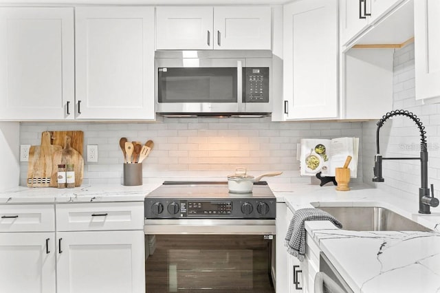 kitchen with backsplash, white cabinets, sink, appliances with stainless steel finishes, and light stone counters