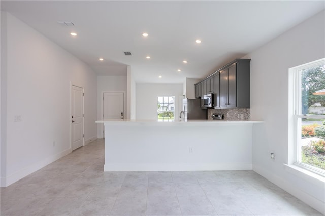 kitchen featuring kitchen peninsula, decorative backsplash, stainless steel appliances, and light tile patterned floors