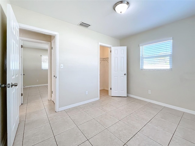 unfurnished bedroom with a walk in closet, a closet, light tile patterned floors, and multiple windows