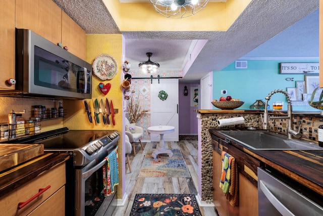 kitchen featuring sink, light wood-type flooring, a textured ceiling, appliances with stainless steel finishes, and a tray ceiling