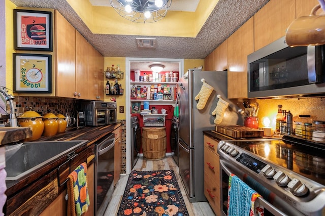 kitchen featuring sink, a textured ceiling, appliances with stainless steel finishes, and light hardwood / wood-style flooring