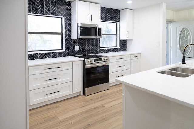 kitchen with stainless steel appliances, white cabinetry, sink, and backsplash