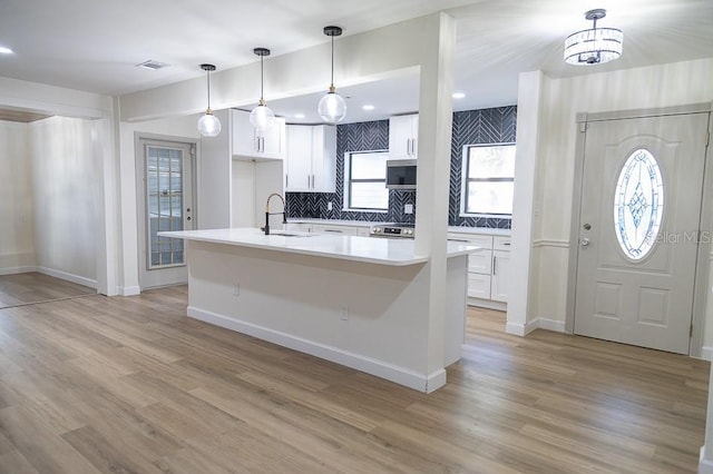 kitchen with hanging light fixtures, sink, white cabinets, and light wood-type flooring