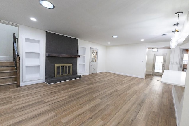 unfurnished living room with wood-type flooring, built in features, and a brick fireplace