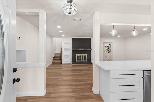 kitchen with white cabinetry, a brick fireplace, light wood-type flooring, and decorative light fixtures