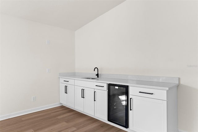 bar with sink, light hardwood / wood-style flooring, beverage cooler, and white cabinets