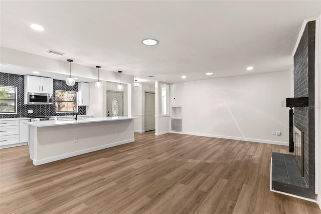 kitchen featuring hardwood / wood-style floors, white cabinets, a center island with sink, a brick fireplace, and decorative light fixtures