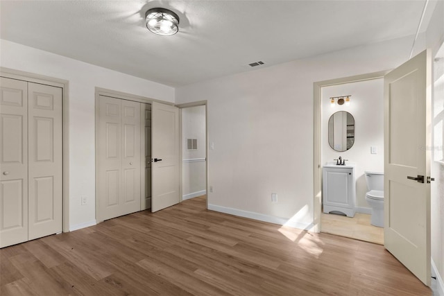 unfurnished bedroom featuring connected bathroom, hardwood / wood-style floors, sink, and multiple closets