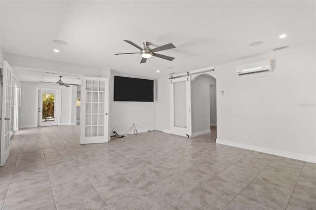 spare room featuring french doors, a barn door, a wall unit AC, and ceiling fan