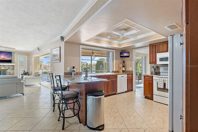 kitchen featuring a breakfast bar, a raised ceiling, white appliances, and kitchen peninsula