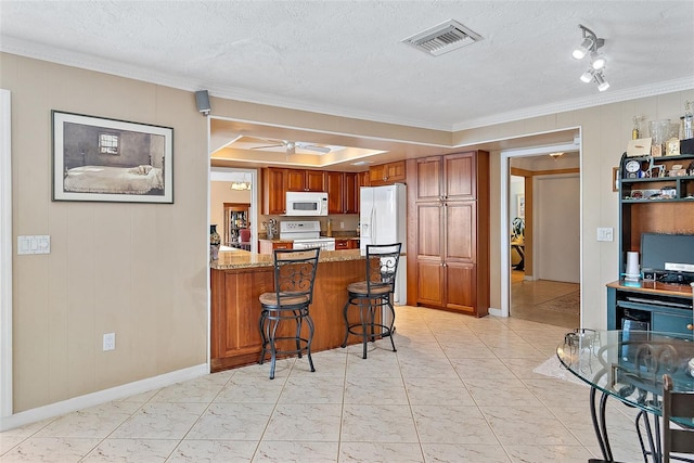 kitchen featuring white appliances, a kitchen breakfast bar, a textured ceiling, light stone counters, and kitchen peninsula