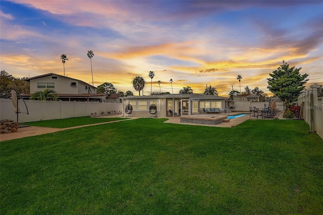 back house at dusk featuring a lawn, a patio area, and a pool