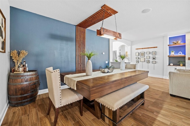 dining space with built in shelves, a textured ceiling, and light hardwood / wood-style floors