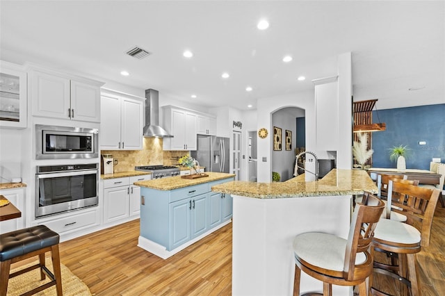 kitchen with wall chimney exhaust hood, a kitchen breakfast bar, light hardwood / wood-style flooring, kitchen peninsula, and appliances with stainless steel finishes