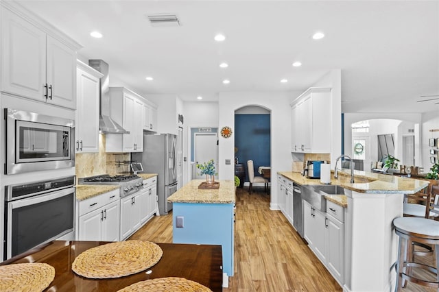 kitchen with kitchen peninsula, light stone counters, stainless steel appliances, and wall chimney range hood