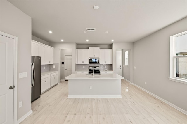 kitchen featuring a wealth of natural light, white cabinetry, decorative backsplash, stainless steel appliances, and a center island with sink