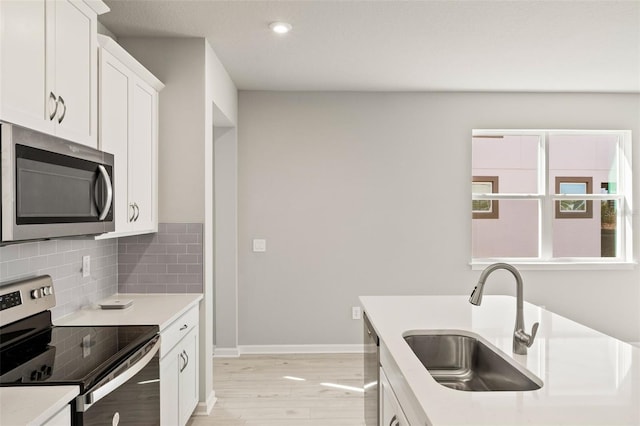 kitchen with sink, white cabinets, decorative backsplash, stainless steel appliances, and light hardwood / wood-style flooring