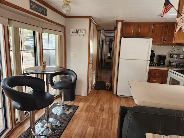 kitchen with a textured ceiling, light hardwood / wood-style floors, white appliances, and crown molding