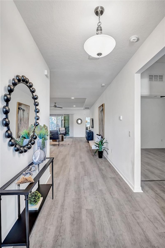 hallway featuring a raised ceiling, a textured ceiling, and light hardwood / wood-style flooring