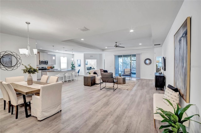 living room featuring a raised ceiling, light hardwood / wood-style floors, and ceiling fan with notable chandelier