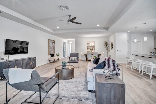 living room featuring light wood-type flooring, a tray ceiling, and ceiling fan