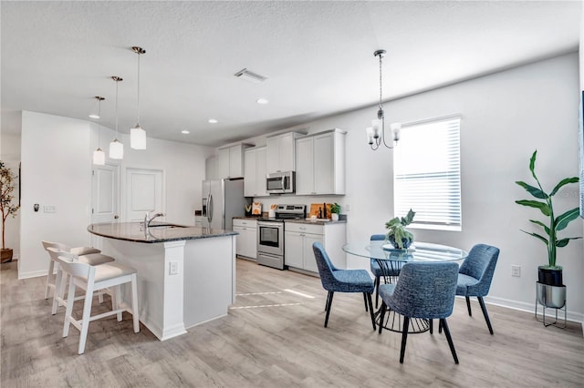 kitchen with sink, dark stone countertops, a center island with sink, white cabinets, and appliances with stainless steel finishes