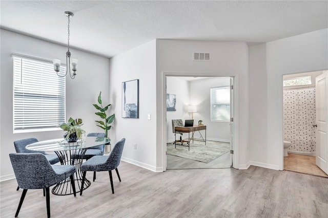 dining room with a textured ceiling, light hardwood / wood-style floors, and a notable chandelier