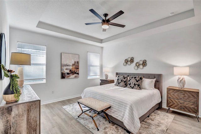 bedroom featuring ceiling fan, light wood-type flooring, and a tray ceiling