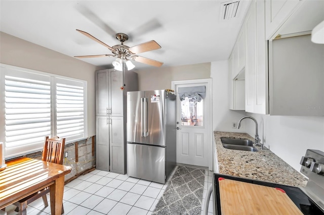 kitchen with light stone counters, stainless steel appliances, ceiling fan, sink, and light tile patterned floors