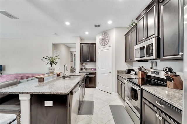 kitchen with light stone countertops, sink, stainless steel appliances, an island with sink, and a breakfast bar