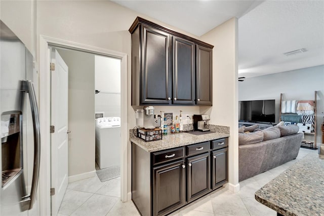 kitchen with stainless steel refrigerator with ice dispenser, washer / dryer, dark brown cabinets, and light tile patterned flooring