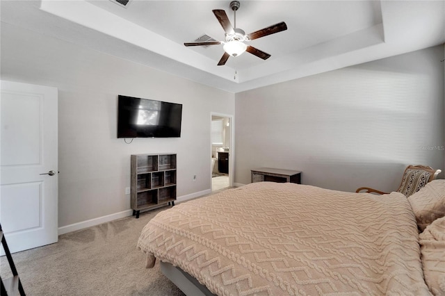 carpeted bedroom with a raised ceiling, connected bathroom, and ceiling fan