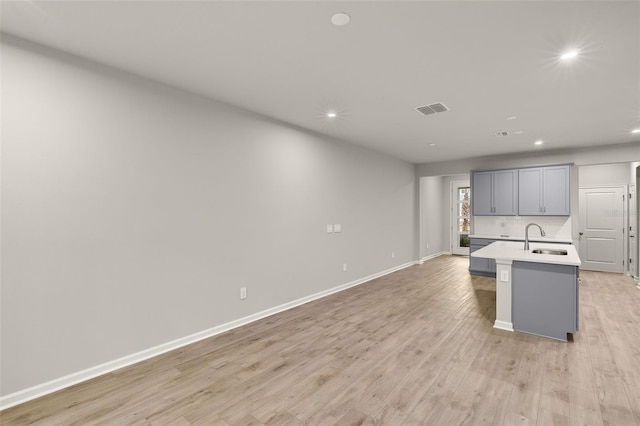 kitchen featuring gray cabinets, an island with sink, sink, decorative backsplash, and light hardwood / wood-style flooring