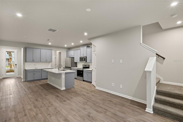 kitchen with gray cabinets, wood-type flooring, appliances with stainless steel finishes, and a kitchen island with sink