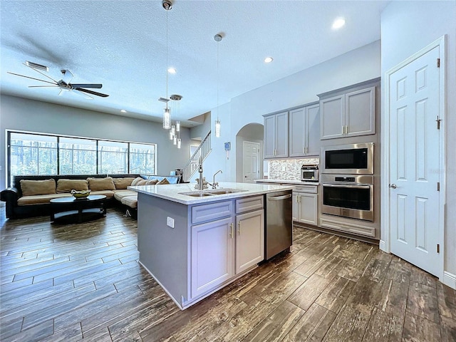 kitchen with gray cabinetry, sink, stainless steel appliances, decorative light fixtures, and a center island with sink