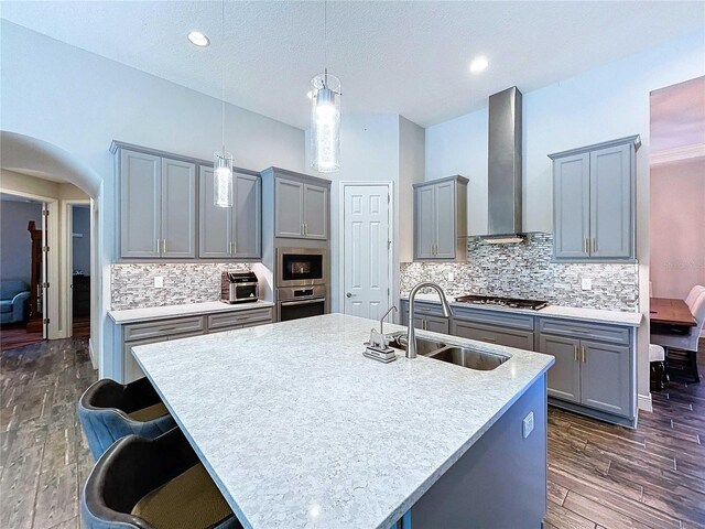 kitchen with dark hardwood / wood-style flooring, hanging light fixtures, wall chimney range hood, and sink