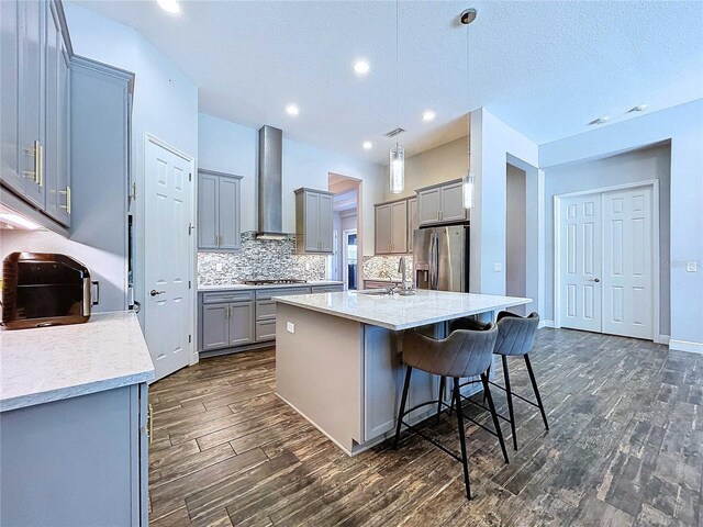 kitchen featuring stainless steel appliances, wall chimney range hood, dark hardwood / wood-style flooring, an island with sink, and pendant lighting