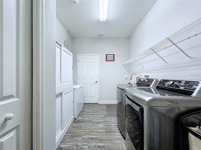 clothes washing area with washing machine and clothes dryer, cabinets, dark wood-type flooring, and a textured ceiling